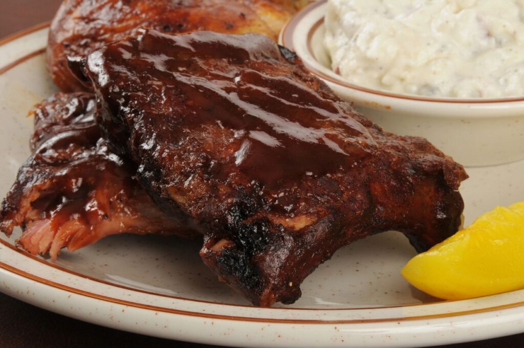 A plate with barbecue ribs, a lemon wedge, and a side of creamy sauce.