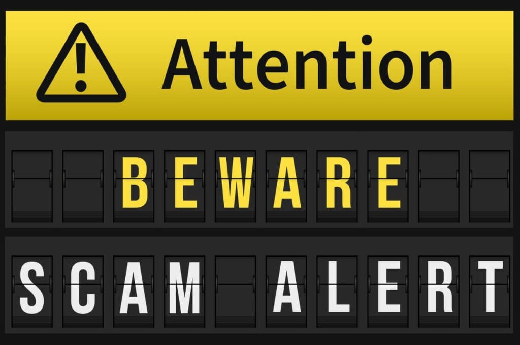 Yellow and black sign reading "Attention: Beware Scam Alert" with exclamation mark symbol.