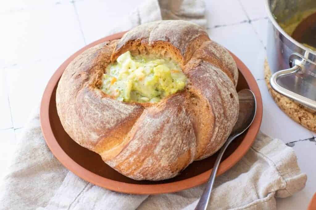 Broccoli Cheddar Soup in a Sourdough Bowl with spoon on a round brown plate.