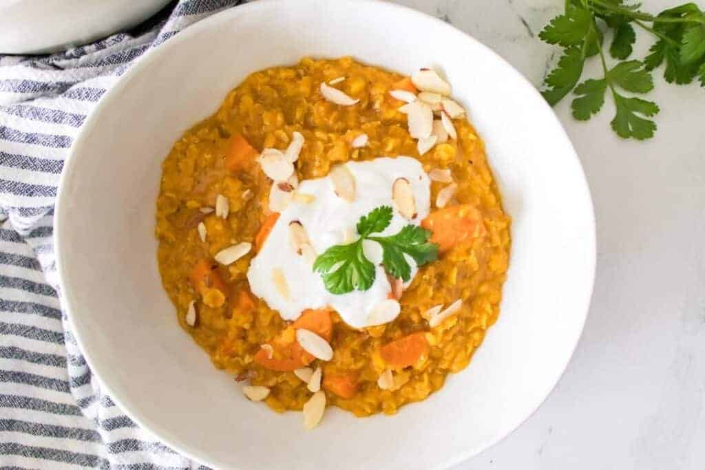 A bowl of carrot and lentil soup topped with yogurt, cilantro, and almond slices.