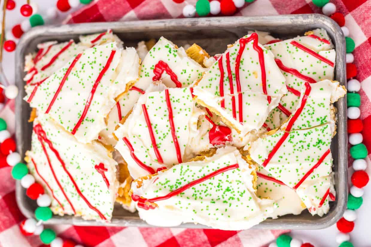 A festive tray of Christmas Tree Cake Crack, featuring broken pieces of white chocolate-coated crackers, topped with red drizzle and green sprinkles.