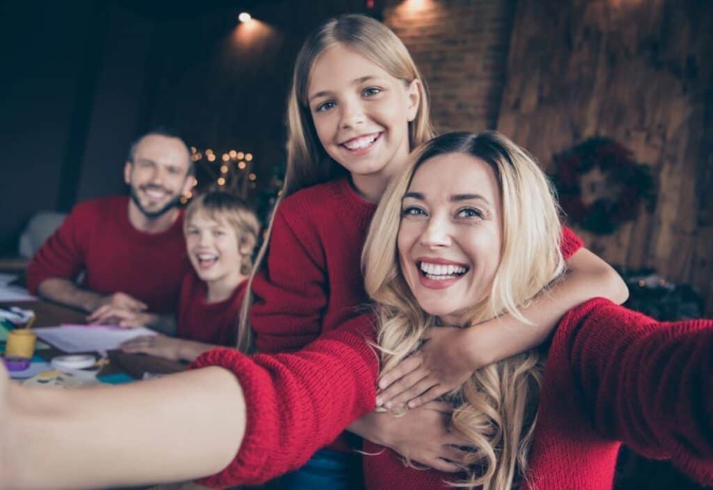 A smiling family of four wearing red sweaters takes a selfie indoors.