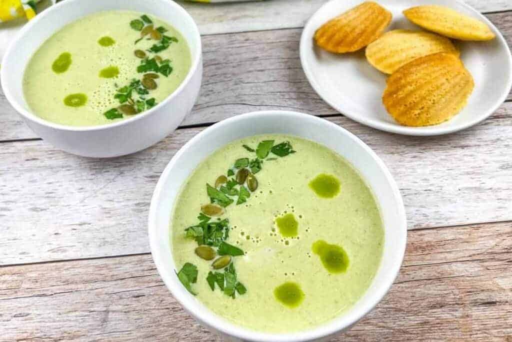 Two bowls of Cream of Jalapeno Soup with a plate of cornbread madeleines on a wooden table.