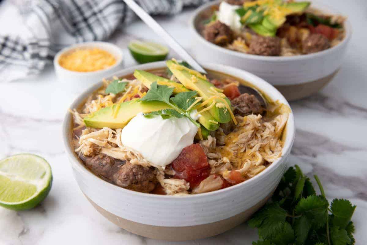 Two bowls of Slow-Cooker Taco Soup next to sliced lime.