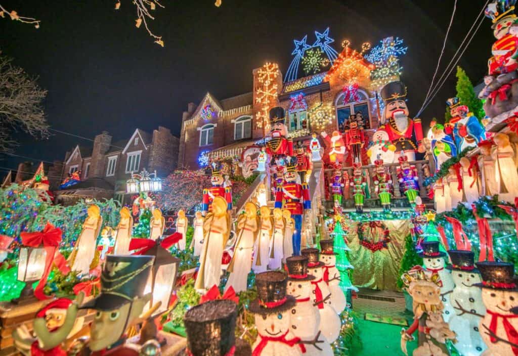 A house is brightly decorated with numerous Christmas lights, nutcrackers, snowmen, and various festive figures on the lawn and roof at night.