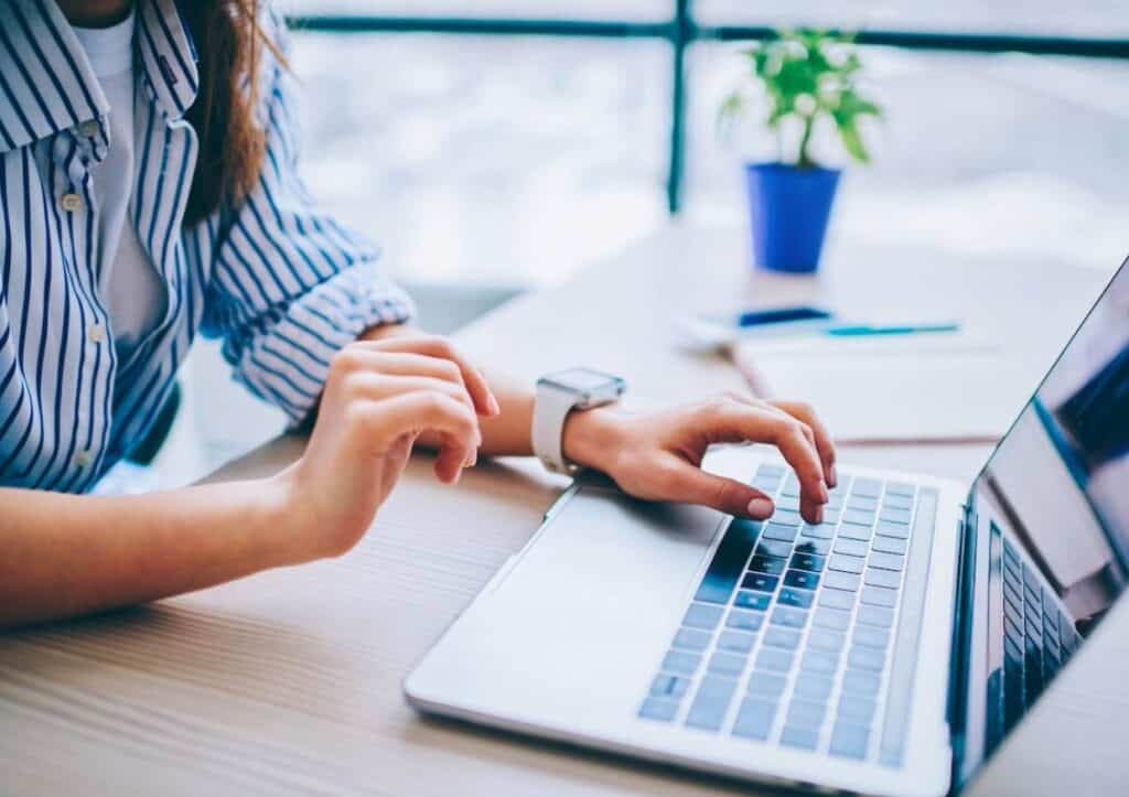 A person in a striped shirt is thoughtfully using a laptop at their desk, surrounded by a small plant and notebook, possibly exploring AI for travel planning to streamline their next adventure.