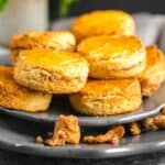 A stack of golden brown scones sits on a dark gray plate, with crumbs scattered around them.