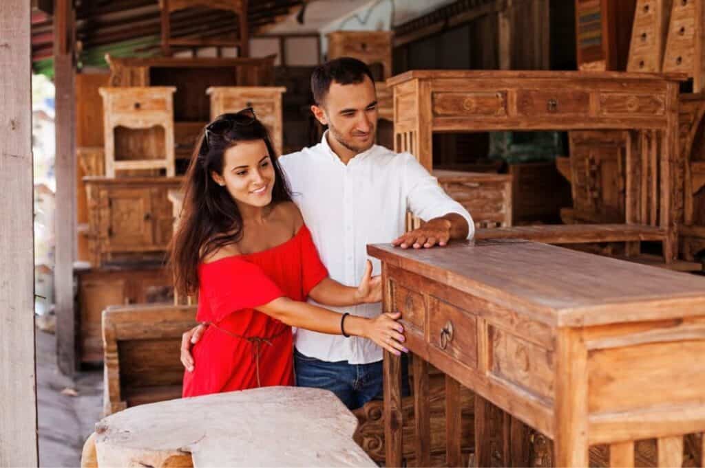 A couple examines wooden furniture at an outdoor market.