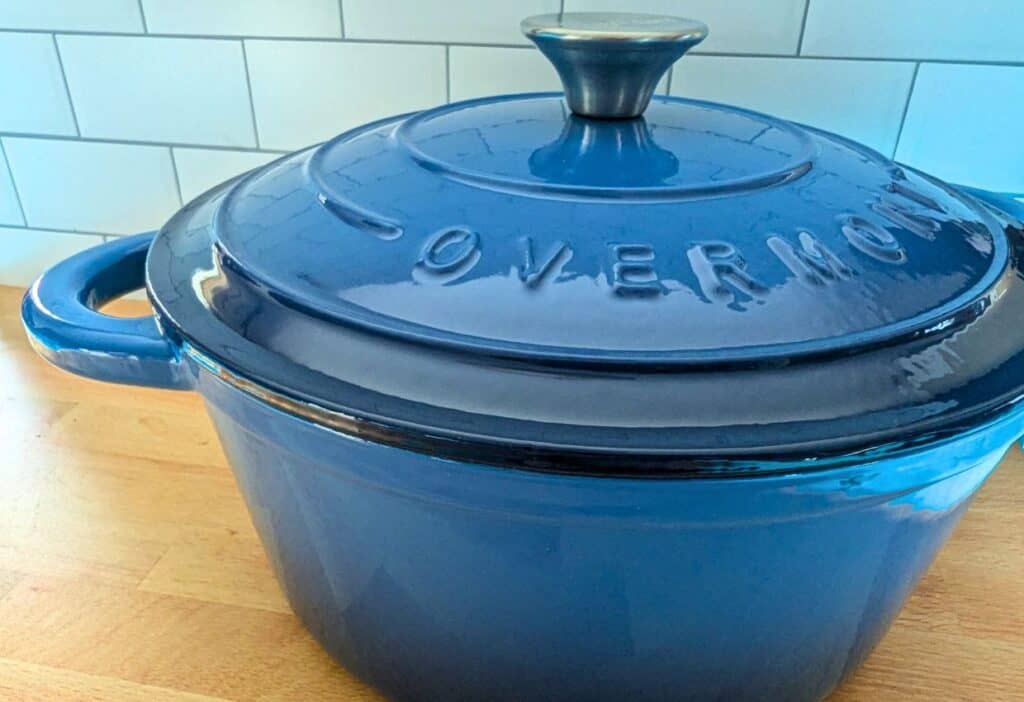 A blue enameled Dutch oven with a handle on the lid, placed on a wooden countertop.