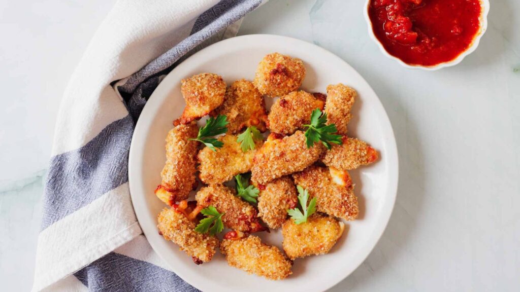 A plate of breaded, fried mozzarella sticks garnished with parsley, accompanied by a small bowl of marinara sauce.