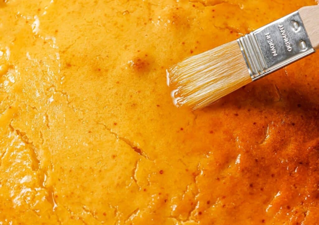 Close-up of a brush applying a glaze to a golden-brown pastry surface.