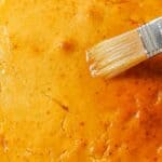 Close-up of a brush applying a glaze to a golden-brown pastry surface.