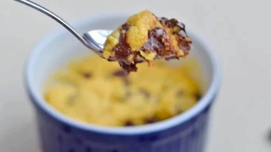 A spoonful of yellow cake with chocolate chips is held above a blue mug, perfect for savoring as one of the delightful New Year's Eve desserts.