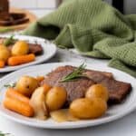 Plates with sliced beef, baby carrots, potatoes, and onions garnished with rosemary. Green cloth in the background.