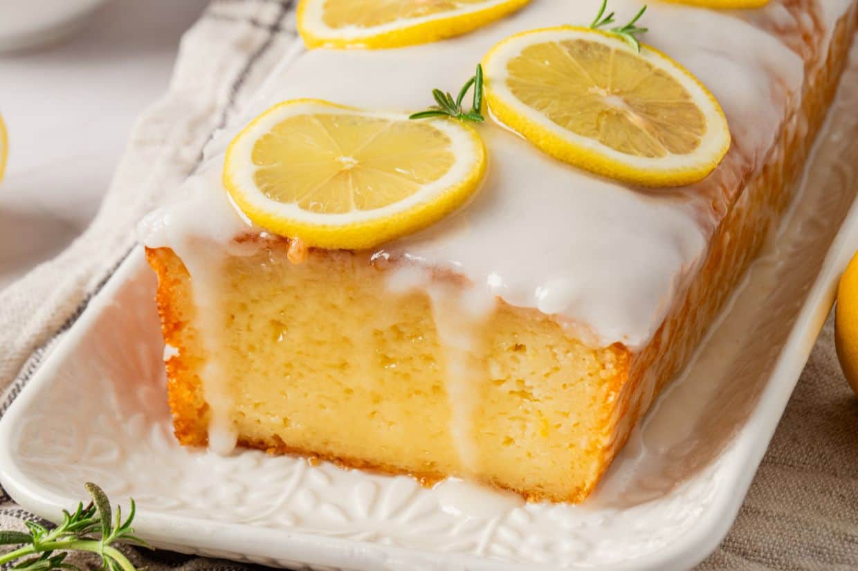 A freshly baked lemon loaf cake, served on a plate and topped with lemon slices.