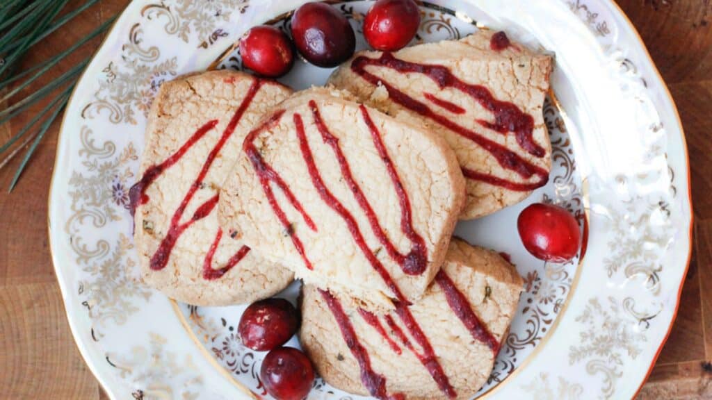 A plate with cookies drizzled with red icing, surrounded by whole cranberries.