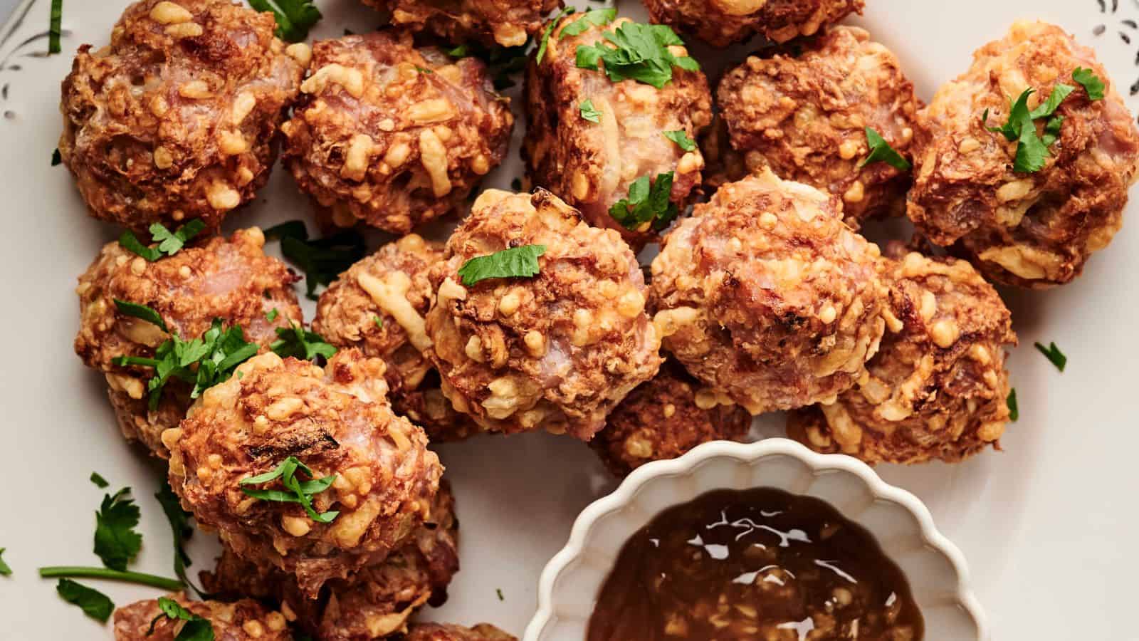 Meatballs garnished with chopped herbs are arranged on a plate next to a small dish of dipping sauce.