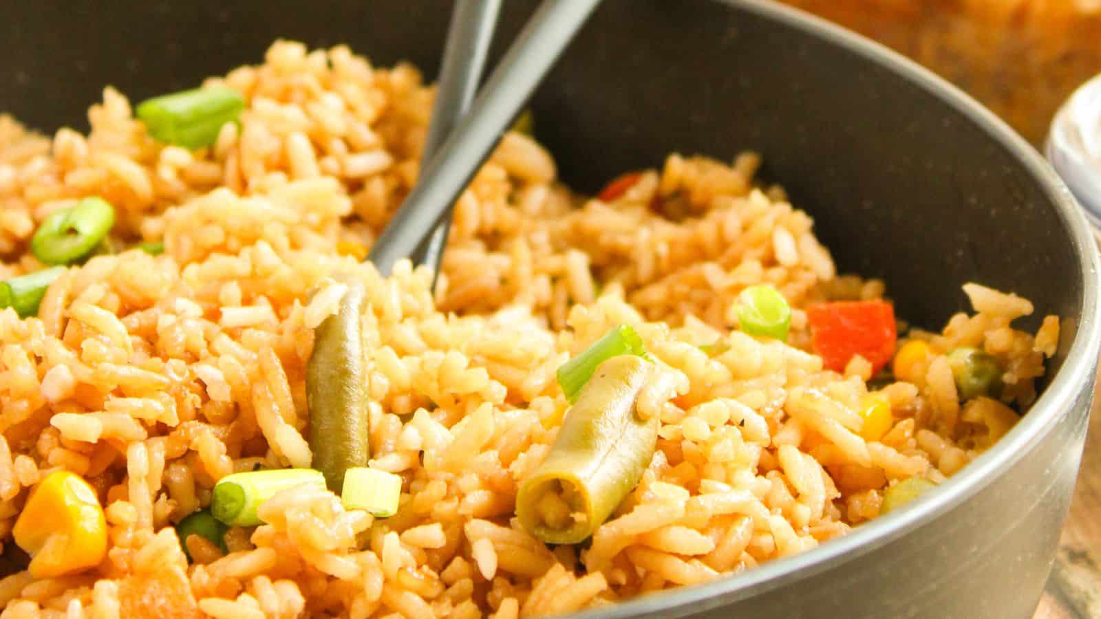 A close-up of a bowl of oven-baked fried rice mixed with colorful vegetables like green beans, bell peppers, and scallions, with a spoon resting inside.