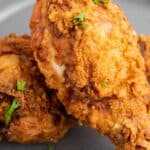 Two pieces of crispy fried chicken garnished with fresh parsley on a gray plate.