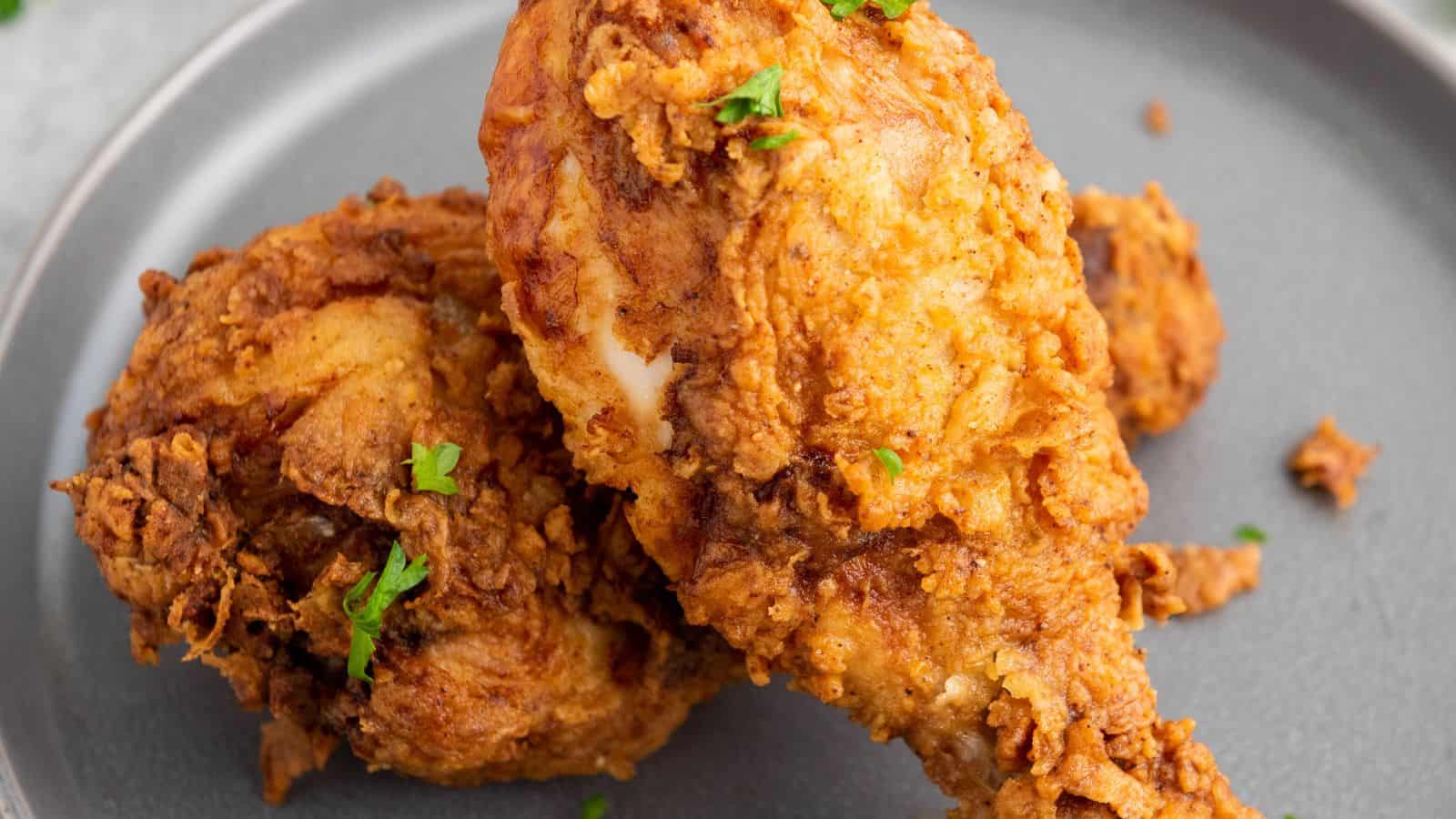 Two pieces of fried chicken on a gray plate, garnished with small bits of green herbs.