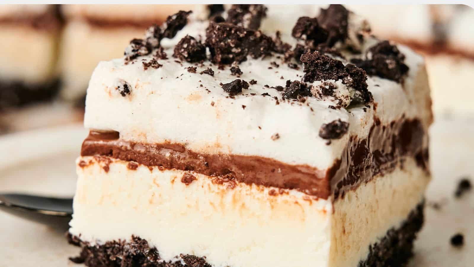 A slice of layered dessert with a creamy white layer, chocolate filling, and crushed cookie topping.