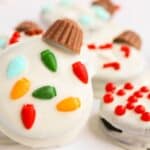 White chocolate-covered cookies decorated with colorful candy lights and red sprinkles, topped with mini chocolate cups.