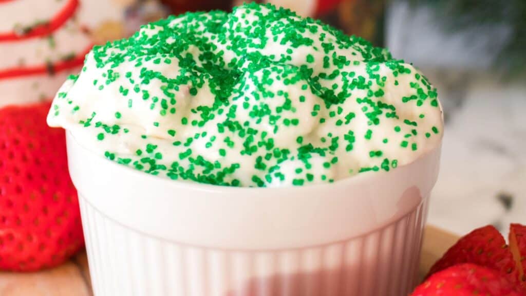 White bowl with creamy dessert topped with green sprinkles, surrounded by fresh strawberries.