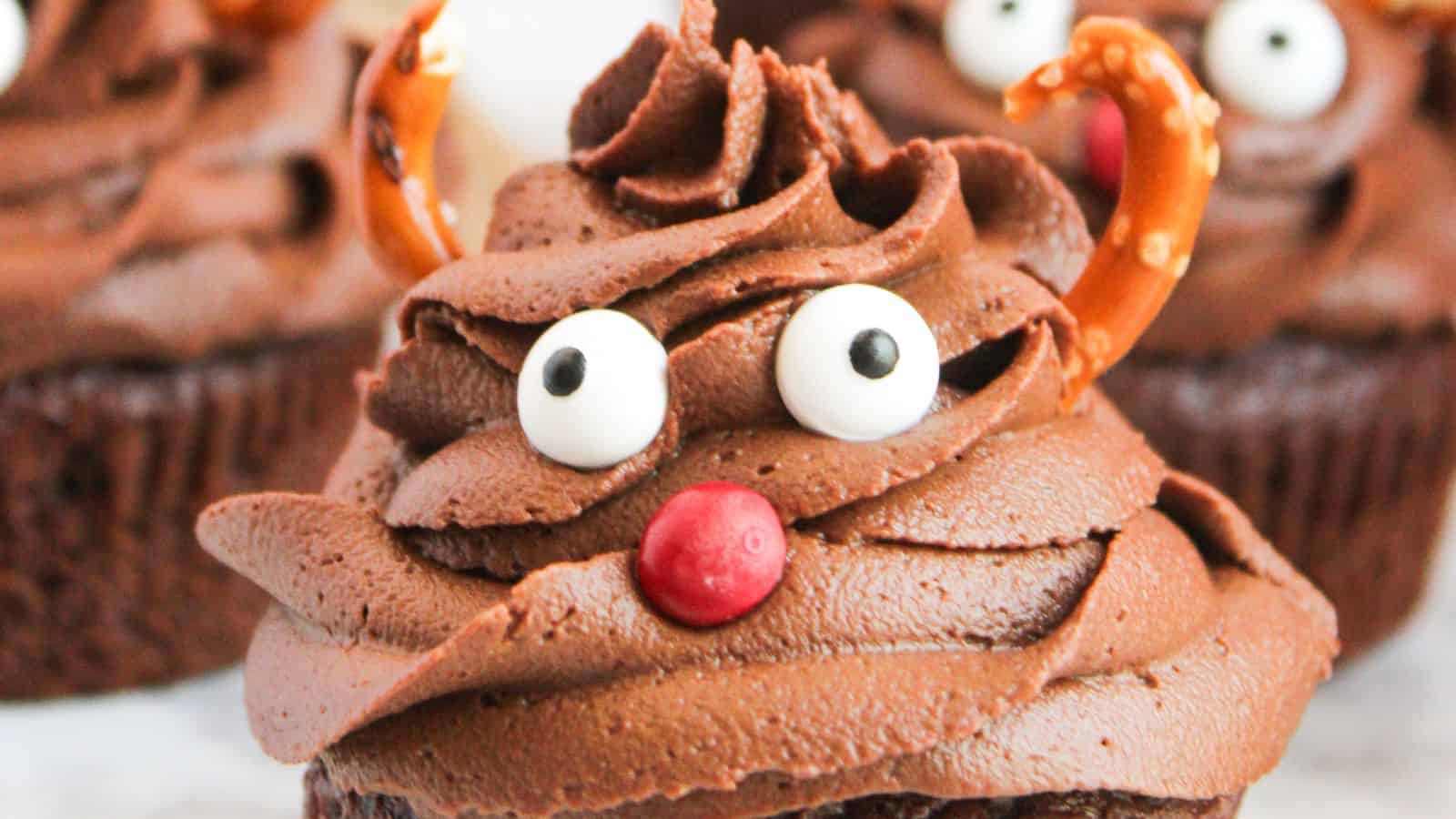 Rudolph cupcakes featuring swirled frosting, candy eyes, a red candy nose, and pretzel antlers mimic the playful charm of a reindeer.