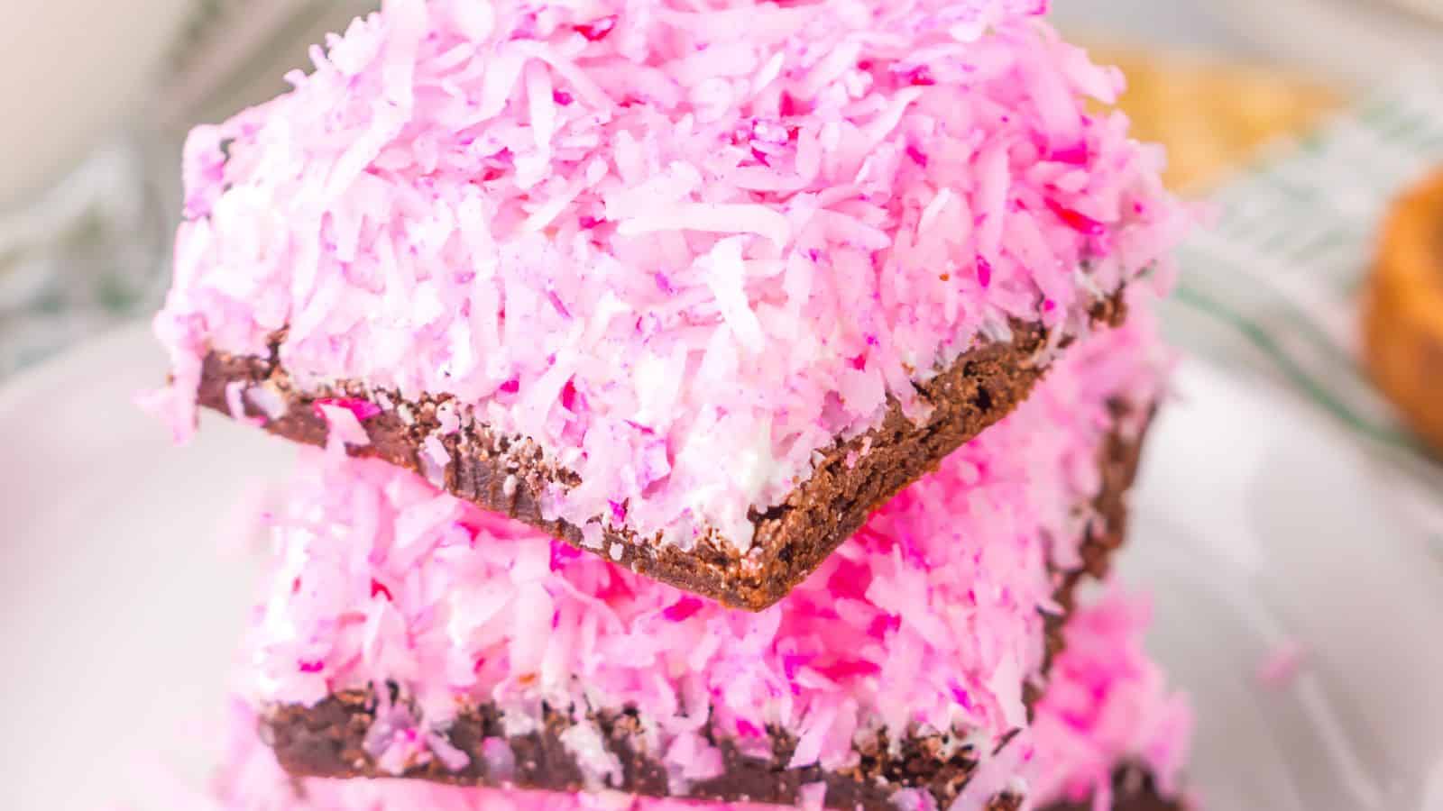 Three stacked slices of chocolate coconut candy, reminiscent of Pink Snoball Brownies, topped with pink shredded coconut.