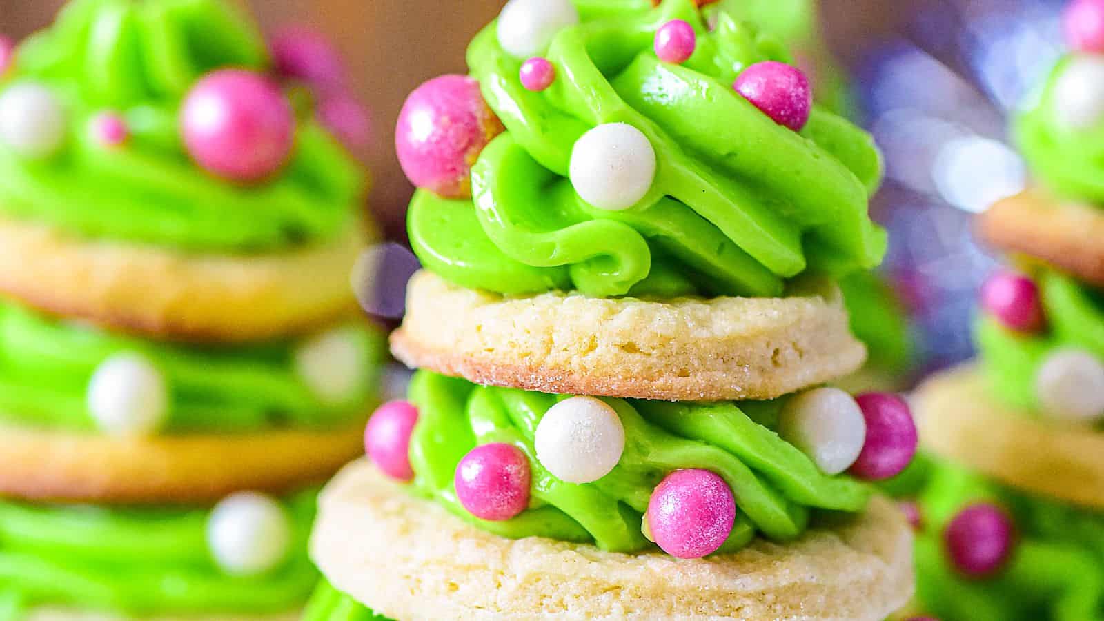 A festive cookie stack resembling a Christmas tree, decorated with green frosting and pink and white edible pearls.
