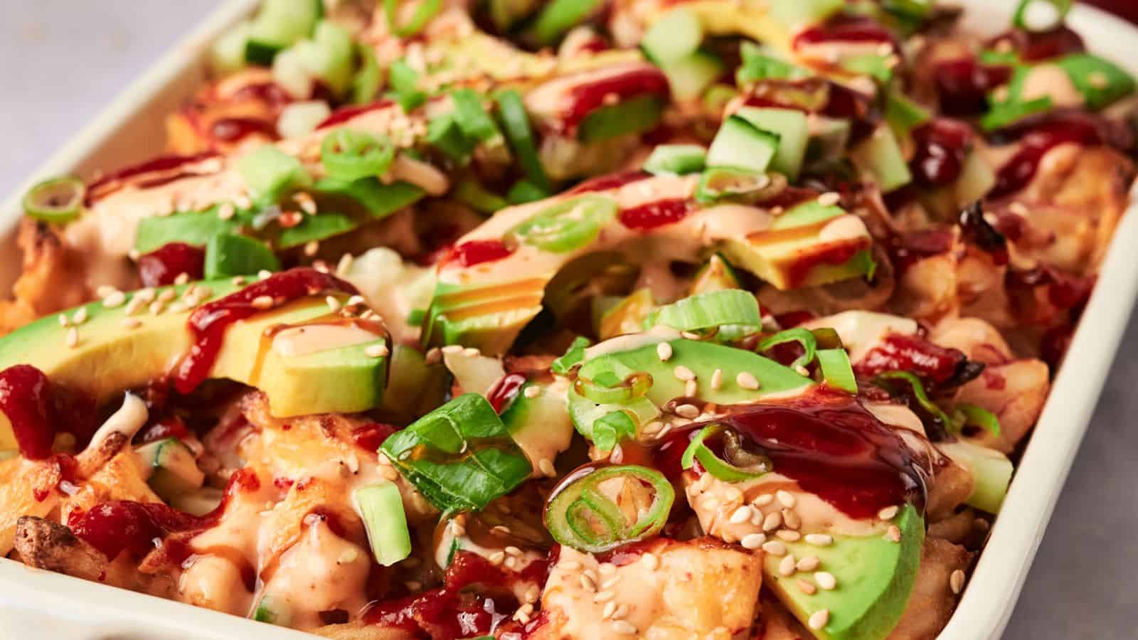 A dish of loaded fries inspired by sushi bake, topped with avocado slices, diced cucumbers, green onions, sesame seeds, and drizzled with sauce.