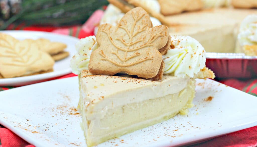 A slice of cream pie topped with a leaf-shaped cookie and whipped cream, surrounded by a sprinkle of cinnamon.