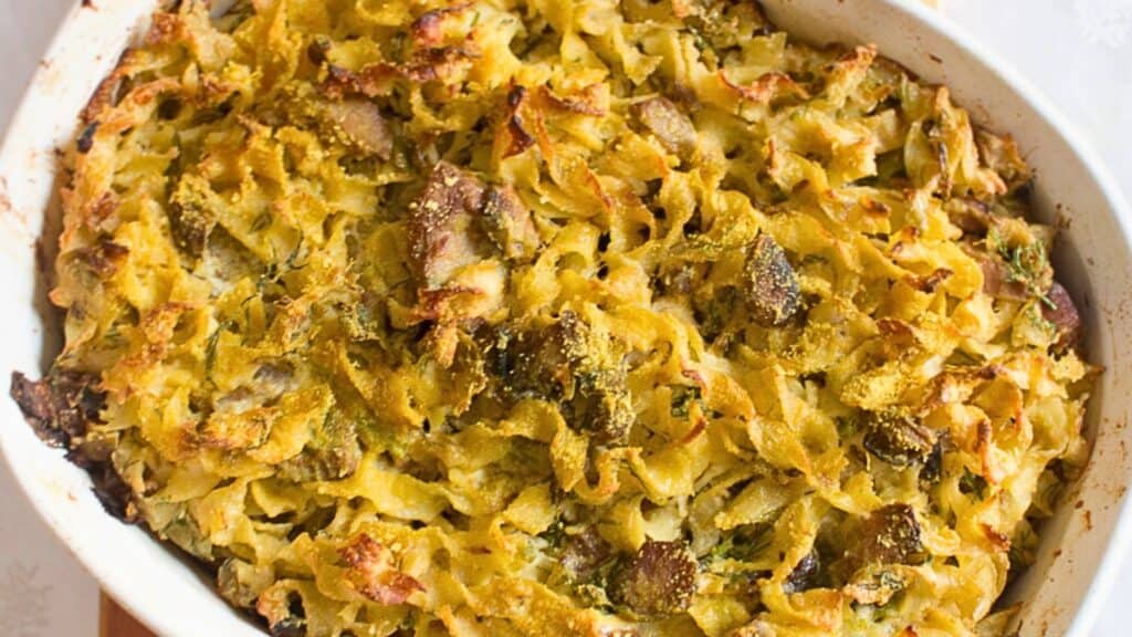 A baked noodle casserole with crispy edges and chunks of meat in a white oval dish.