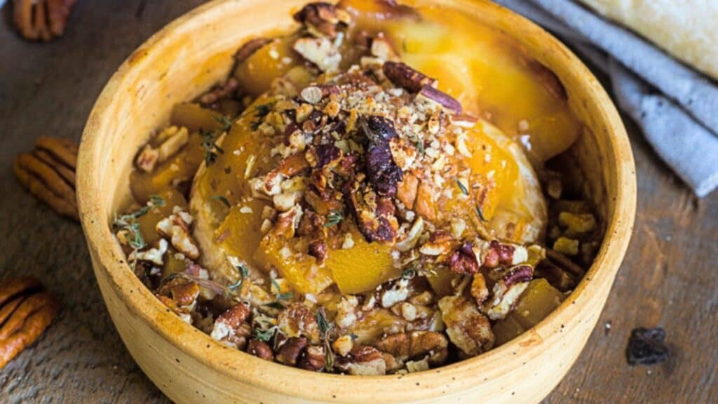 A wooden bowl filled with roasted squash pieces topped with chopped pecans and herbs.