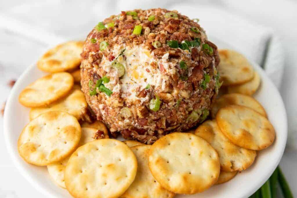 A Pecan Bacon cheese ball coated with nuts and herbs on a white plate.