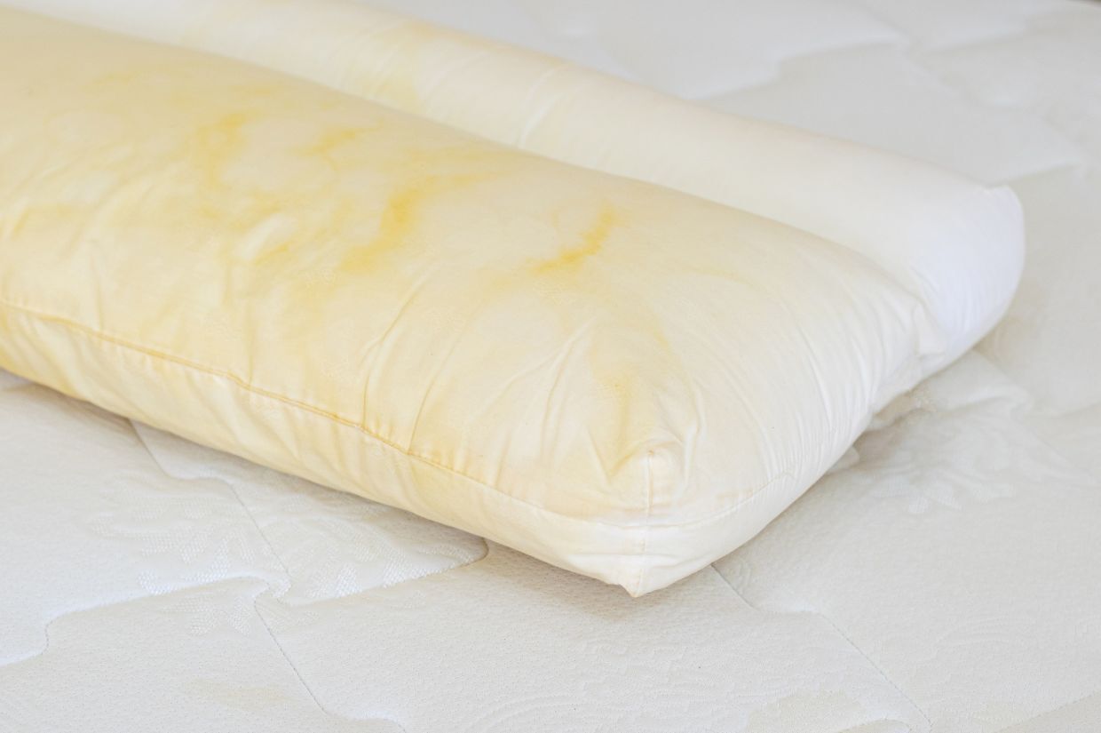 Pillow with yellow stains on a white mattress.