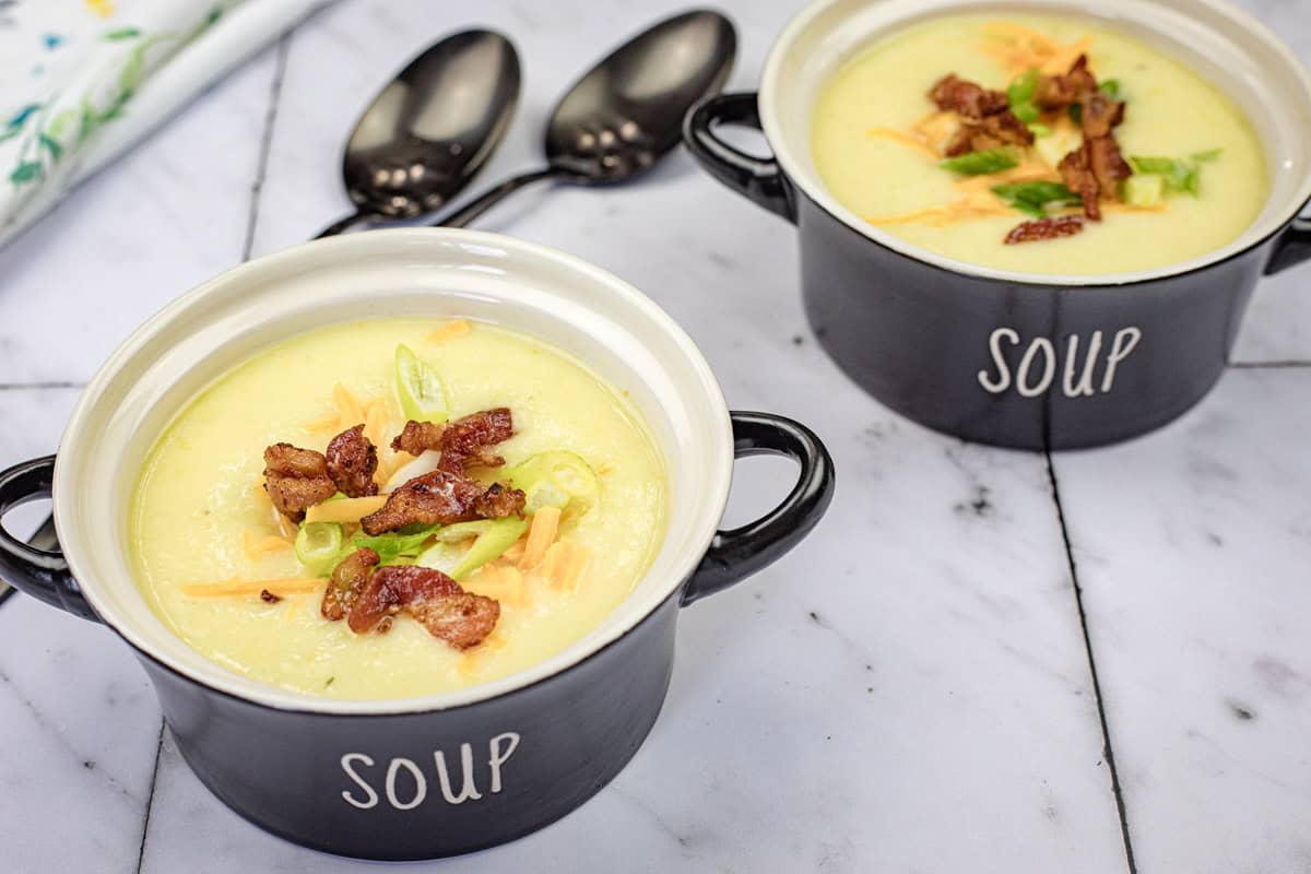 Two bowls of Potato leek soup with two spoons beside them on a tile.