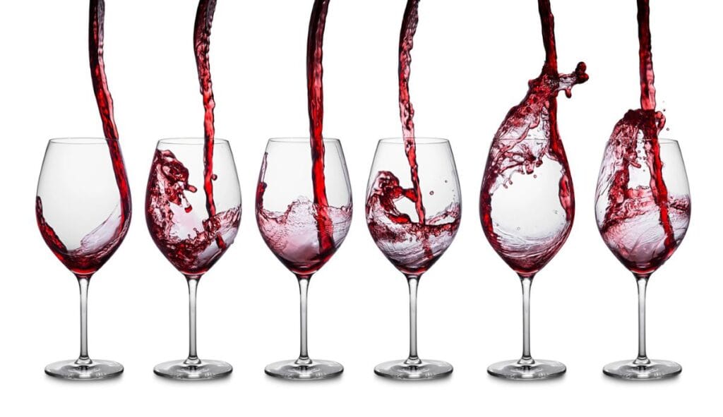 Red wine being poured into six wine glasses, capturing various stages of splashing and filling.