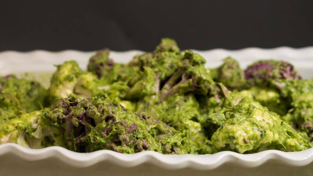 A dish of cauliflower florets covered in green pesto sauce on a white scalloped platter.