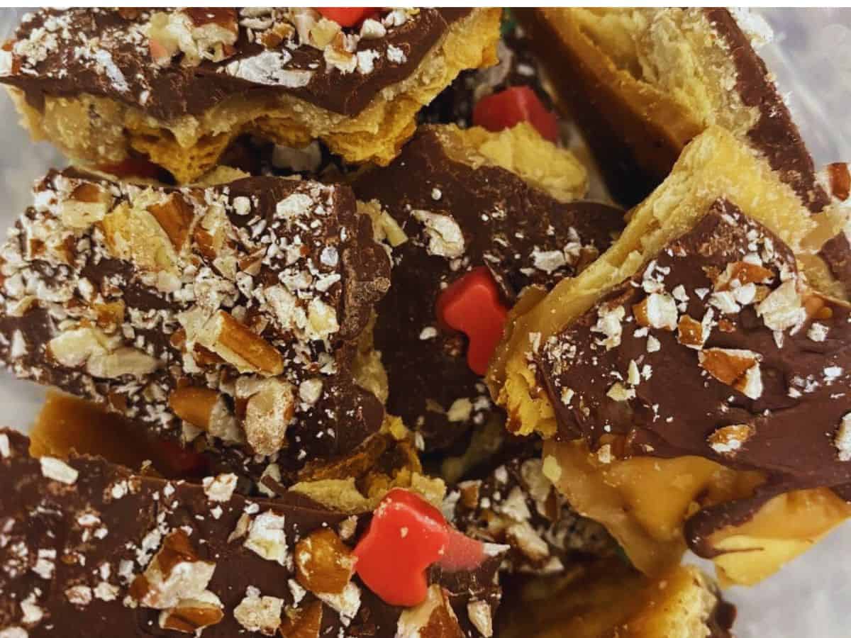 Close-up of toffee pieces topped with chocolate, crushed nuts, and red heart-shaped sprinkles.