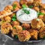 A plate of grilled meatballs garnished with herbs surrounds a bowl of creamy sauce with a dill topping.