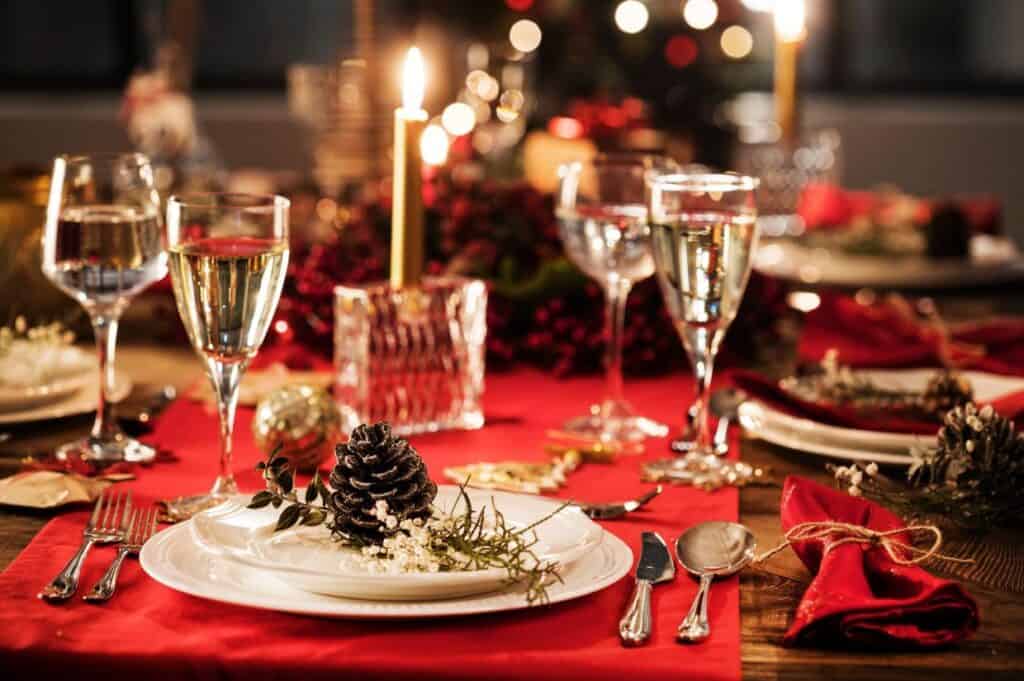 A festive table set for a celebration, with wine glasses and red napkins arranged elegantly around a pine cone centerpiece. A lit candle adds warmth, creating a serene escape from holiday stress.