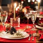 A festive table set for a celebration, with wine glasses and red napkins arranged elegantly around a pine cone centerpiece. A lit candle adds warmth, creating a serene escape from holiday stress.