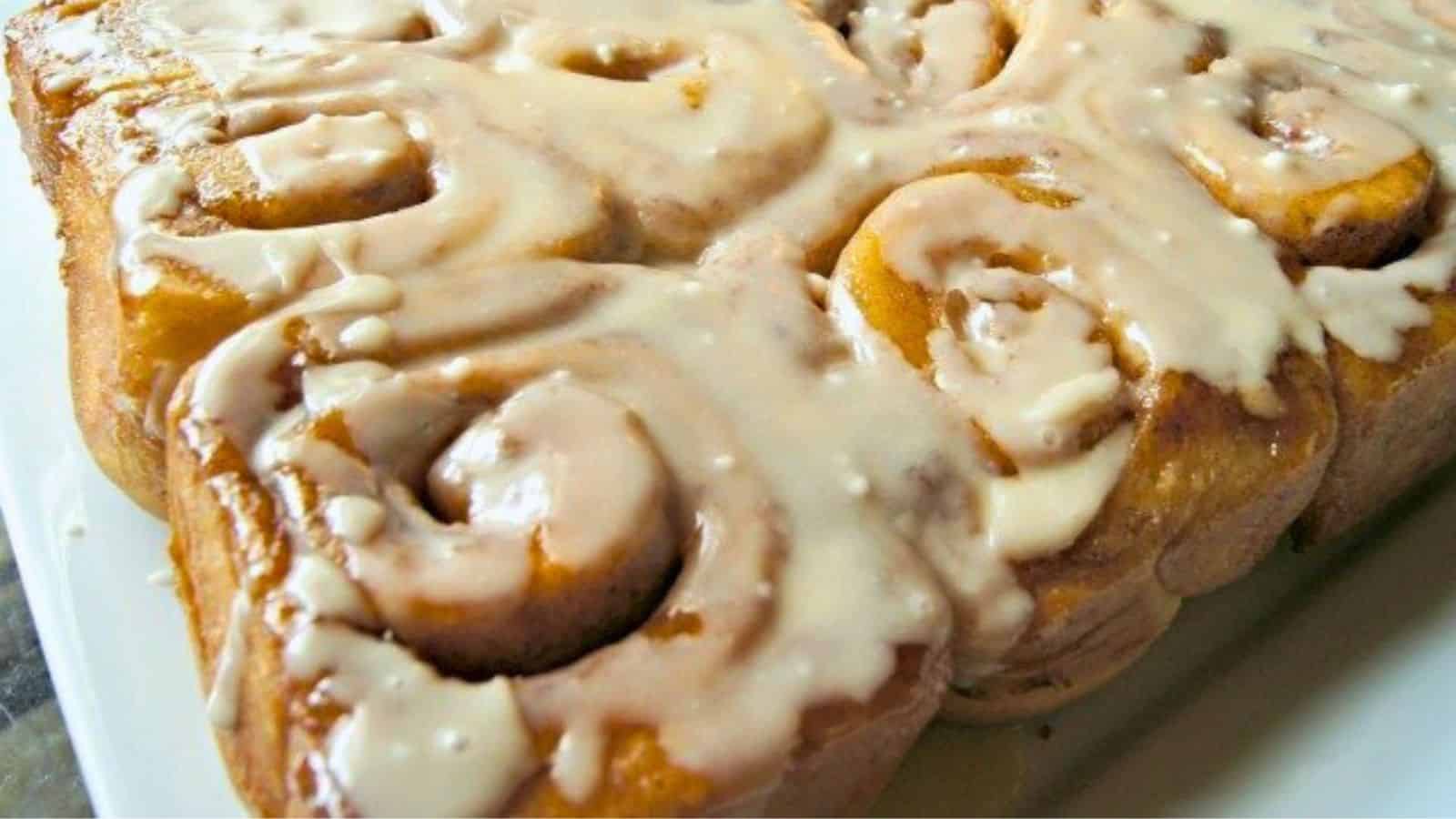 Image shows a batch of freshly baked cinnamon rolls topped with icing on a white plate.