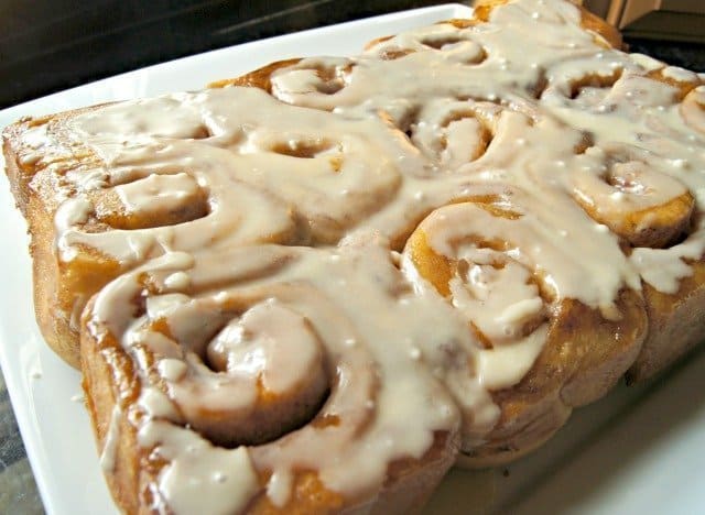 A plate of freshly baked cinnamon rolls topped with white icing.