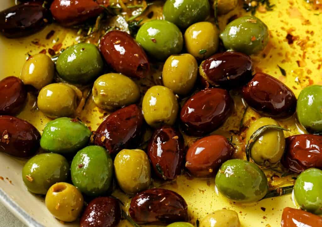 A mix of green and brown olives marinated in oil, herbs, and spices.