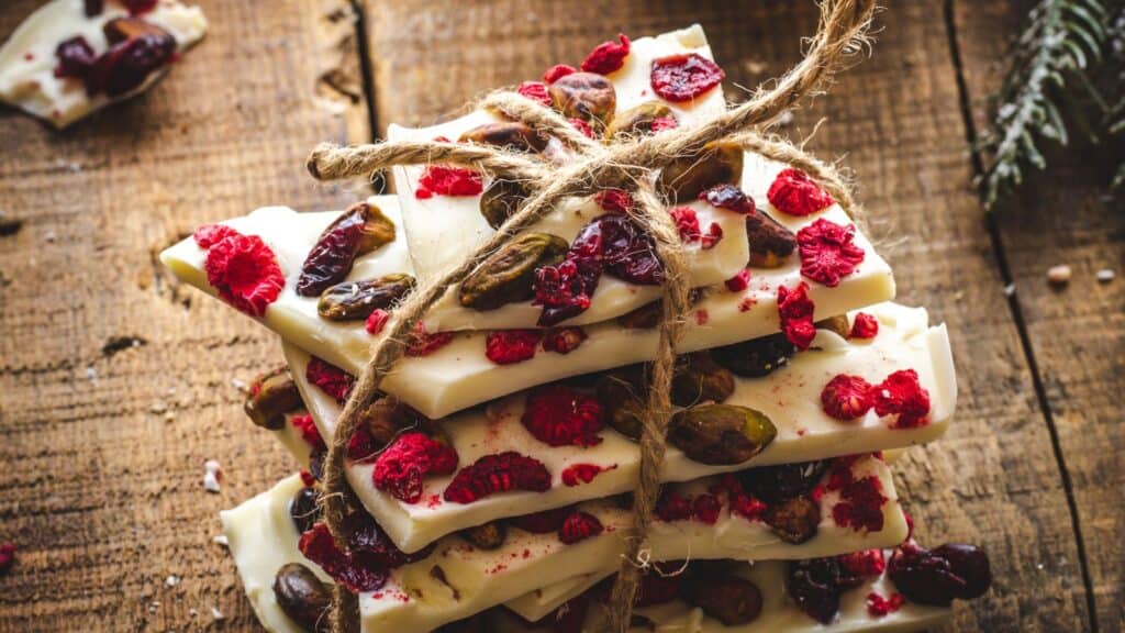 Stack of homemade white chocolate bark with dried raspberries, cranberries, and nuts, tied with twine, on a rustic wooden surface.