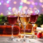 Four wine glasses filled with red and white wine are arranged on a table alongside a bottle, capturing the essence of an elegant wine pairing. Festive decorations surround them, with blurred colorful lights creating a vibrant background ambience.