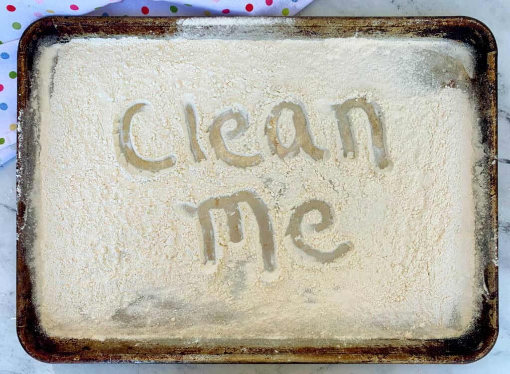 A dusty baking tray with the words "Clean Me" written in the dust.