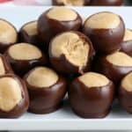 A plate of chocolate-covered peanut butter balls, with one of them partially eaten, revealing the creamy peanut butter filling inside.